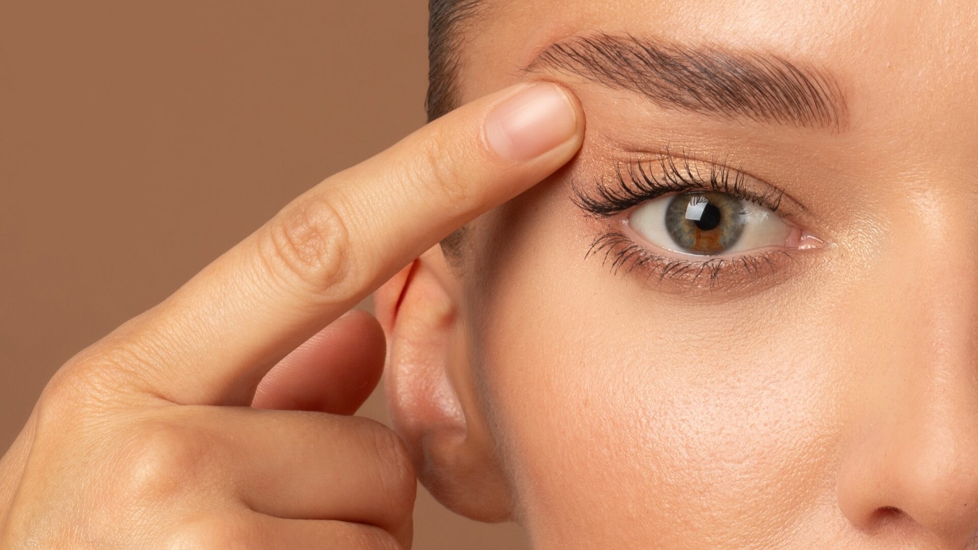 Closeup of young European woman pointing to the wrinkles on the upper eyelid, touching face. Blepharoplasty concept