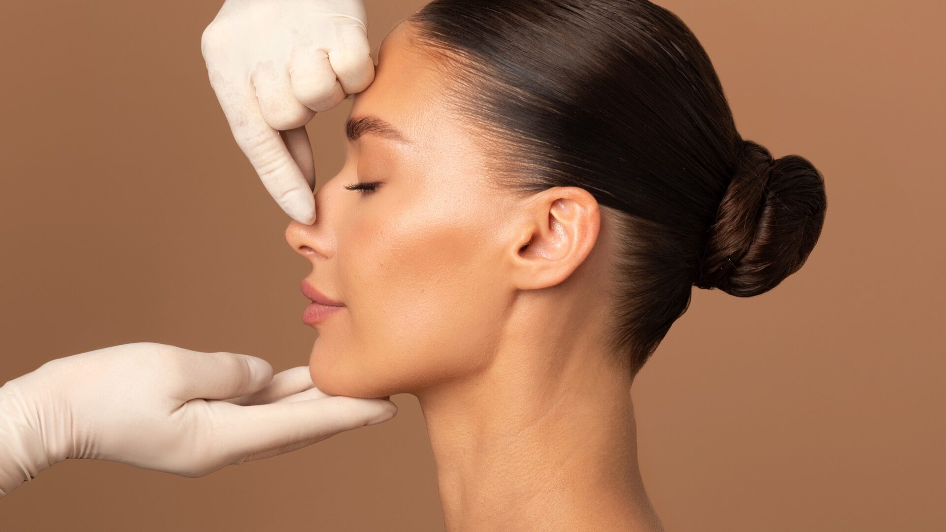 Plastic surgery and beauty concept. Surgeon touching woman nose, consulting before rhinoplasty operation on brown background, side view